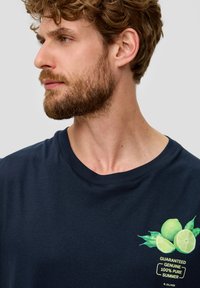 Marineblauwe katoenen T-shirt met een grafisch ontwerp van limoenen en bladeren met een tekstlabel, ronde halslijn en korte mouwen.