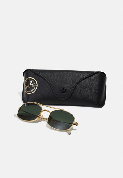Lunettes de soleil Ray-Ban avec verres verts et monture en métal doré, posées à côté d'un étui noir texturé avec un logo et un fermoir à pression.