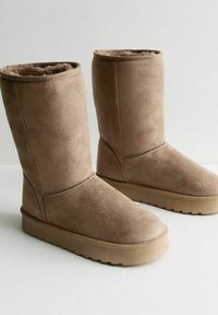 Bruna mocka ankelstövlar med en platt gummisula, mjuk foder och en enkel design med sydda detaljer på sidorna.