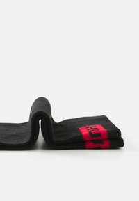Calcetines negros con un diseño plegado, que presentan un detalle de logotipo en un vibrante color rosa. Están fabricados con una suave tela texturizada, con puños reforzados y costuras lisas.