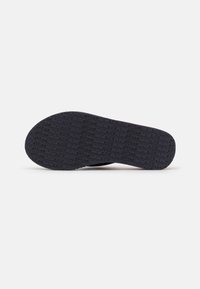 Black rubber shoe sole featuring a textured surface with embossed branding. The design is flat and slightly rounded at the toe.
