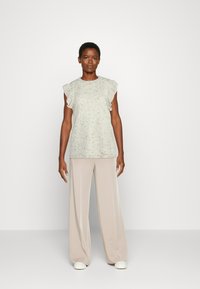 Top de malha cinza claro com mangas franzidas, combinado com calças largas beiges e sapatos brancos de deslizar. Textura suave, design casual.
