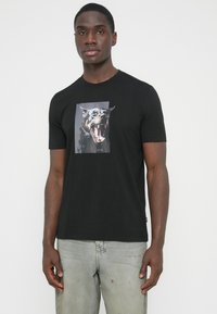 Črna bombažna majica s potiskano sliko lajajočega psa na sprednji strani. Kratki rokavi in okrogla izrez na vratu.
