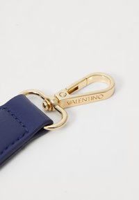 Curea din piele de culoare bleu marin cu o cataramă de culoare aurie, având logo-ul gravat „Valentino” și un element metalic circular, detaliu de cusătură vizibil.