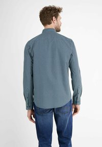 Langdurige mouwen shirt in donkerteal met kleine witte stippen; standaard kraag; rechte snit; gecombineerd met blauwe spijkerbroek; textuurstof.