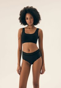 Czarny stanik braletka z kwadratowym dekoltem i szerokimi ramiączkami, zestawiony z dopasowanymi majtkami z wysokim stanem z koronkowym wykończeniem i falbankami.