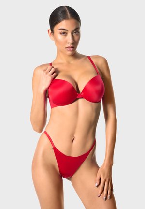 Czerwony zestaw biustonosza i stringów z miękkiego, elastycznego materiału. Biustonosz posiada regulowane ramiączka i elegancki fason podkreślający kształt.
