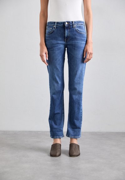 Lyseblå denimjeans med lige pasform, fem lomme-design og subtil falmning. Kombineret med mørke vævede mules.