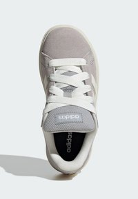 Šedé semišové a síťované tenisky s bílými tkaničkami, vybavené polstrovaným jazykem a detaily loga. Podešev je béžová a má zaoblený tvar špičky.