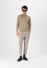 Ανοιχτό μπεζ πουλόβερ, γκρι πλισέ παντελόνι και μαύρα παπούτσια; μοντέ�λο που φορά στρογγυλά γυαλιά ηλίου; απαλές υφές και χαλαρή εφαρμογή.