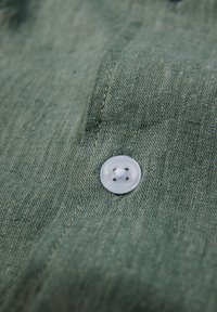 Tela de lino verde con una textura suave, que presenta un botón de plástico transparente con cuatro agujeros, cosechado con hilo a juego.