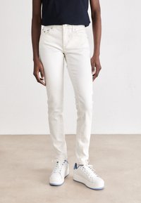 Jeans ajustados beige de mezclilla, con cinco bolsillos, una cintura de altura media, y combinados con zapatillas de plataforma blancas con detalles azules.