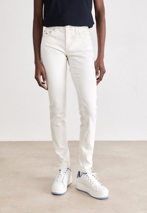 Beige skinny jeans lavet af denim, med fem lommer, en mid-rise talje og parret med hvide platform sneakers med blå accenter.