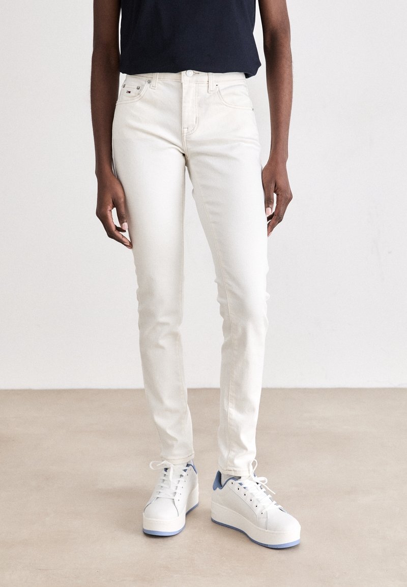 Jeans ajustados beige de mezclilla, con cinco bolsillos, una cintura de altura media, y combinados con zapatillas de plataforma blancas con detalles azules.