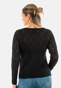 Maglione nero con un motivo a onde texturizzato, maniche lunghe e scollatura ampia. Abbinato a jeans blu con dettagli sulle tasche posteriori.