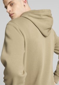 Felpa beige con cappuccio in tessuto testurizzato, vista posteriore, cappuccio prominente e vestibilità morbida. Mostrata su un modello di spalle.