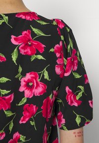 Tecido preto com estampado floral vibrante em rosa, apresentando folhas verdes. Mangas curtas em balão com detalhe texturizado, close-up da área do ombro.