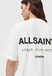 Biała bawełniana, oversize'owa koszulka z dużym czarnym napisem na plecach: "ALLSAINTS", z japońskimi znakami oraz napisem "LONDON" na dole.