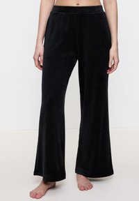 Zwarte fluwelen broek met een wijde pijpdesign, elastische tailleband en zachte textuur. De zoomafwerking is netjes zonder versieringen.