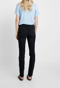 Černé fitted džíny s klasickým pětiokem, s mid-rise pasem a hladkou strukturou, spárované se světle modrým topem.