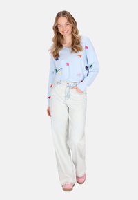 Maglione corto azzurro chiaro con accenti ricamati multicolore, abbinato a jeans a vita alta in lavaggio chiaro e scarpe con plateau rosa.