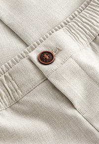 Gros plan sur un pantalon à taille élastique beige avec un bouton marron à quatre trous et des détails de couture visibles.