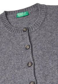 Cárdigan gris de punto con cuello acanalado, cinco botones marrones y una etiqueta verde que dice "United Colors of Benetton" en el cuello.