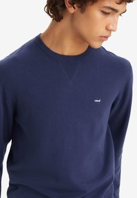 Marineblauwe crewnecktrui van zachte brei stof met geribde manchetten en ronde hals. Bevat een klein Levi's-logo op de borst.