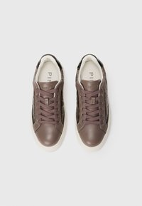 Un paio di sneakers in pelle marrone con lati trapuntati, lacci marroni, bordi neri sul tallone e suole bianche, viste dall'alto.