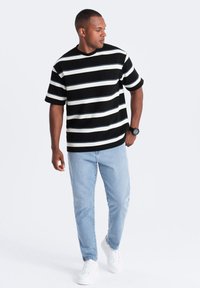 Camisa de manga corta a rayas en blanco y negro combinada con jeans de color azul claro y zapatillas blancas. La camisa tiene un escote redondo y un corte holgado.