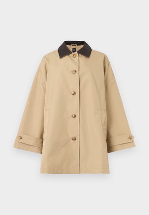 Manteau beige à boutons, manches larges, col marron foncé, poches et poignets boutonnés, présenté sur un fond blanc.