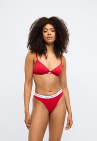 Rød bomulds-bh med tynde stropper og en lukning foran, kombineret med en matchende rød g-streng med en hvid bånd med logo.