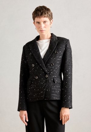Schwarzer doppelt brüstiger Blazer mit glänzenden Sprenkeln, strukturiertem Stoff, Reverskragen und zwei Fronttaschen, kombiniert mit einem weißen Hemd.