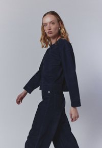 Mornarska žakardna jakna s krojenjem u skraćenom izdanju, dugim rukavima i prednjim džepom, u kombinaciji s odgovarajućim pantalonama visokog struka, glatke teksture.