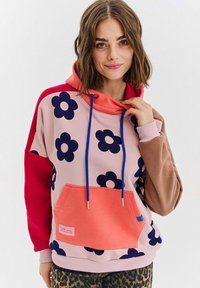 Farebná mikina s kapucňou v ružovej, červenej a hnedej farbe so námorníckymi kvetinovými vzormi. Obsahuje veľkú prednú kapsu, modré šnúrky a rebrované manžety.
