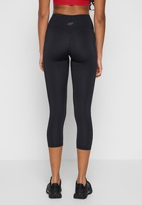 Czarne legginsy typu capri wykonane z elastycznego materiału, z wysokim pasem i małym logo z tyłu. Gładka textura, bez widocznych wzorów.