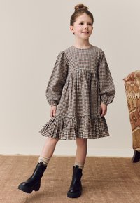 Hnedé a krémové kárované šaty s nafúknutými rukávmi a volánikovým lemom, doplnené čiernymi členkovými čižmami a krémovými ponožkami po kolená.