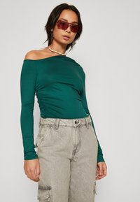 Roheline pika varrukaga blouse pehmest ja venivast materjalist, külgedel kogumise detailidega, kombineerituna heleda halli cargo-pükstega, millel on tasku aktsendid.