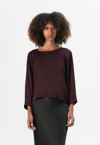 Haut bordeaux à manches chauve-souris avec un col rond, en tissu doux et avec une coupe ample, associé à une jupe crayon noire unie pour le contraste.