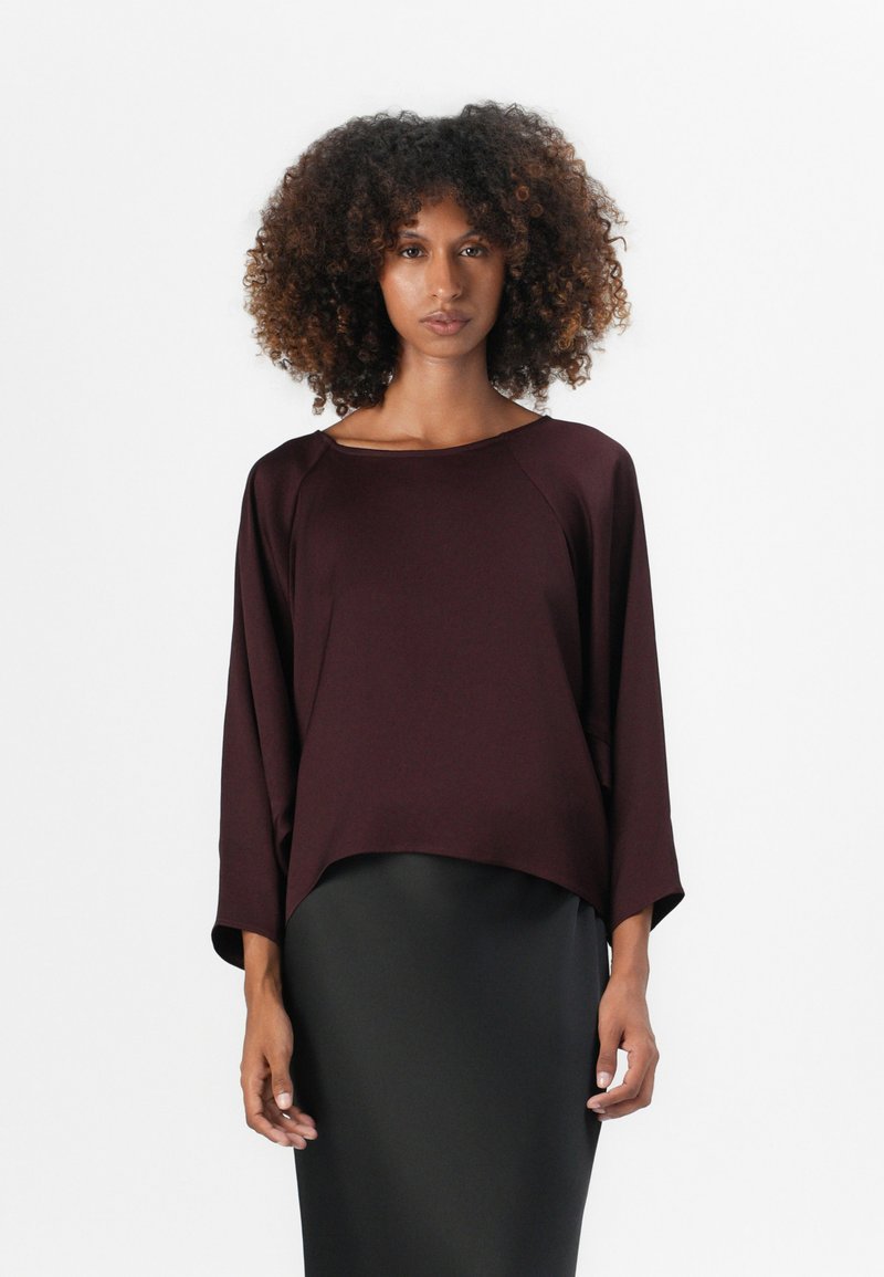 Haut bordeaux à manches chauve-souris avec un col rond, en tissu doux et avec une coupe ample, associé à une jupe crayon noire unie pour le contraste.