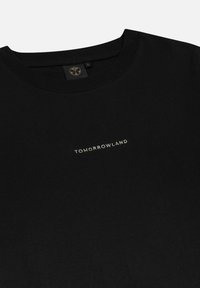 Zwarte katoenen T-shirt met een ronde hals. Bevat een kleine, metalen tekst "TOMORROWLAND" op de borst. Zachte textuur, standaard pasvorm.