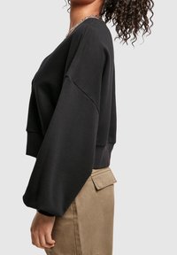 Black cropped sweatshirt with wide sleeves and a rounded neckline. Smooth fabric with a relaxed fit. Paired with beige high-waisted pants.