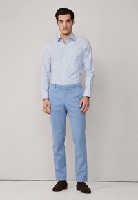 Jasnoniebieskie spodnie w połączeniu z białą koszulą z cienkimi niebieskimi paskami. Spodnie mają gładką fakturę, a koszula jest zapięta pod kołnierzykiem.