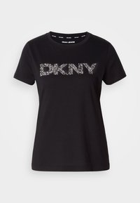 Črna bombažna majica s kratkimi rokavi in krožnim izrezom, z napisom "DKNY" v srebrnih okrasnih detajlih spredaj. Gladka tekstura.