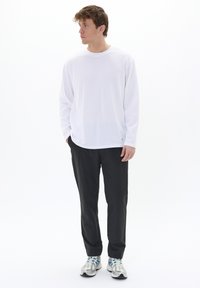 Witte long sleeve shirt gecombineerd met zwarte broek en grijze sneakers met blauwe accenten. Glad materiaal, ontspannen pasvorm en ronde hals.