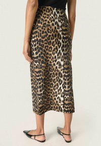 Jupe midi en imprimé léopard noir et or, présentant une texture lisse et une silhouette droite. Fabriquée en tissu léger, avec une fente sur le côté.
