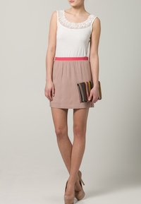 Top de tirantes con encaje blanco, cinturilla elástica rosa, falda beige, combinado con un bolso de mano multicolor y tacones nude. Textura suave.