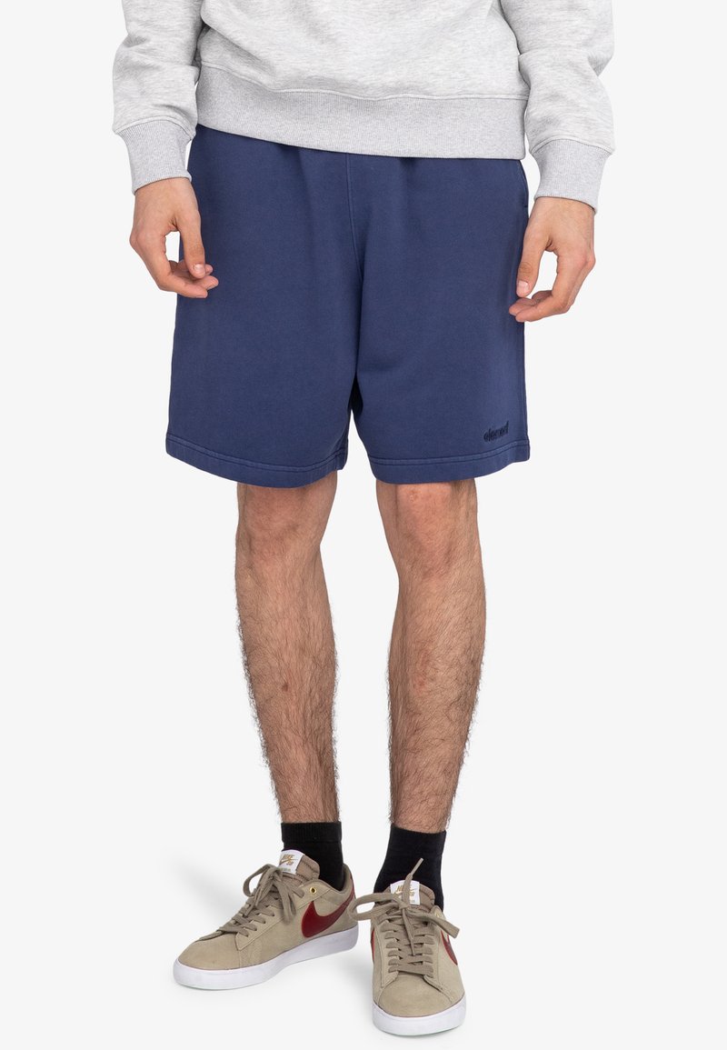 Marine sportshorts gemaakt van zachte stof, met een elastische tailleband en zijzakken. Gecombineerd met een grijze sweater en beige sneakers.