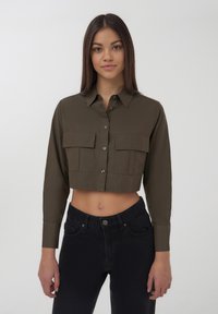 Camicia verde oliva tagliata con maniche lunghe, chiusura con bottoni frontale e due tasche sul petto. Tessuto liscio, con una vestibilità su misura.