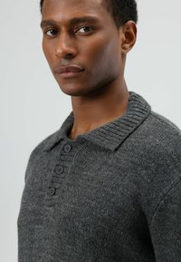 Grijze gebreide trui met een geribde kraag, voorzien van een knoopsluiting met vier donkere knopen, close-up weergave die de textuur en vakmanschap benadrukt.